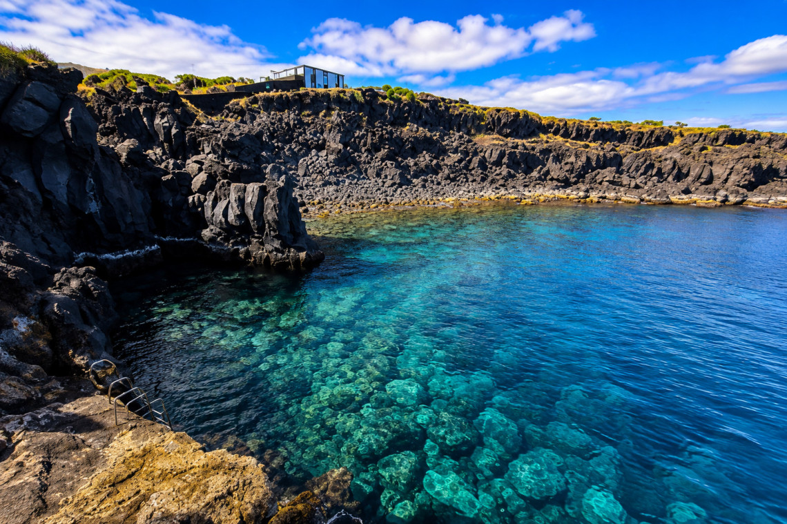 Cachorro natural pool in Bandeiras on Pico Island, with clear Atlantic water enclosed by rugged black volcanic rock formations. The swimming area is part of Pico Island&rsquo;s UNESCO Vineyard Culture landscape.