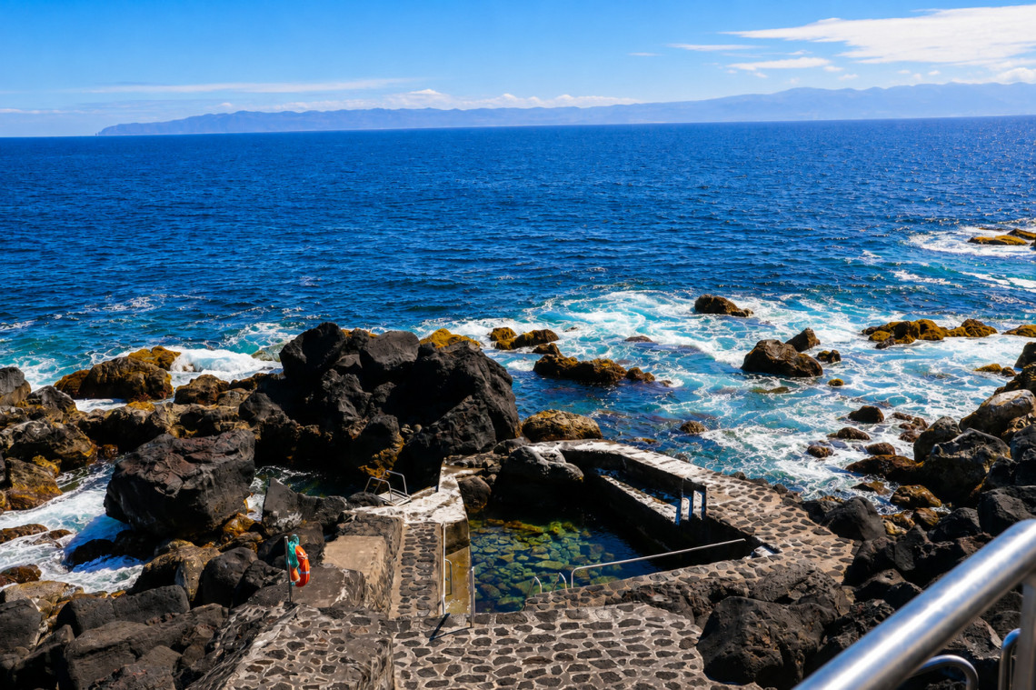 Natural swimming pool in Santa Luzia on Pico Island, enclosed by black volcanic rock beside the Atlantic Ocean. Stone paths and steps provide access to the clear seawater.