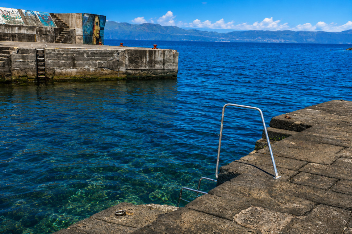 Coastal bathing area in Santo Amaro on Pico Island, with clear Atlantic water, concrete harbor walls and metal swimming ladders providing direct access to the sea.