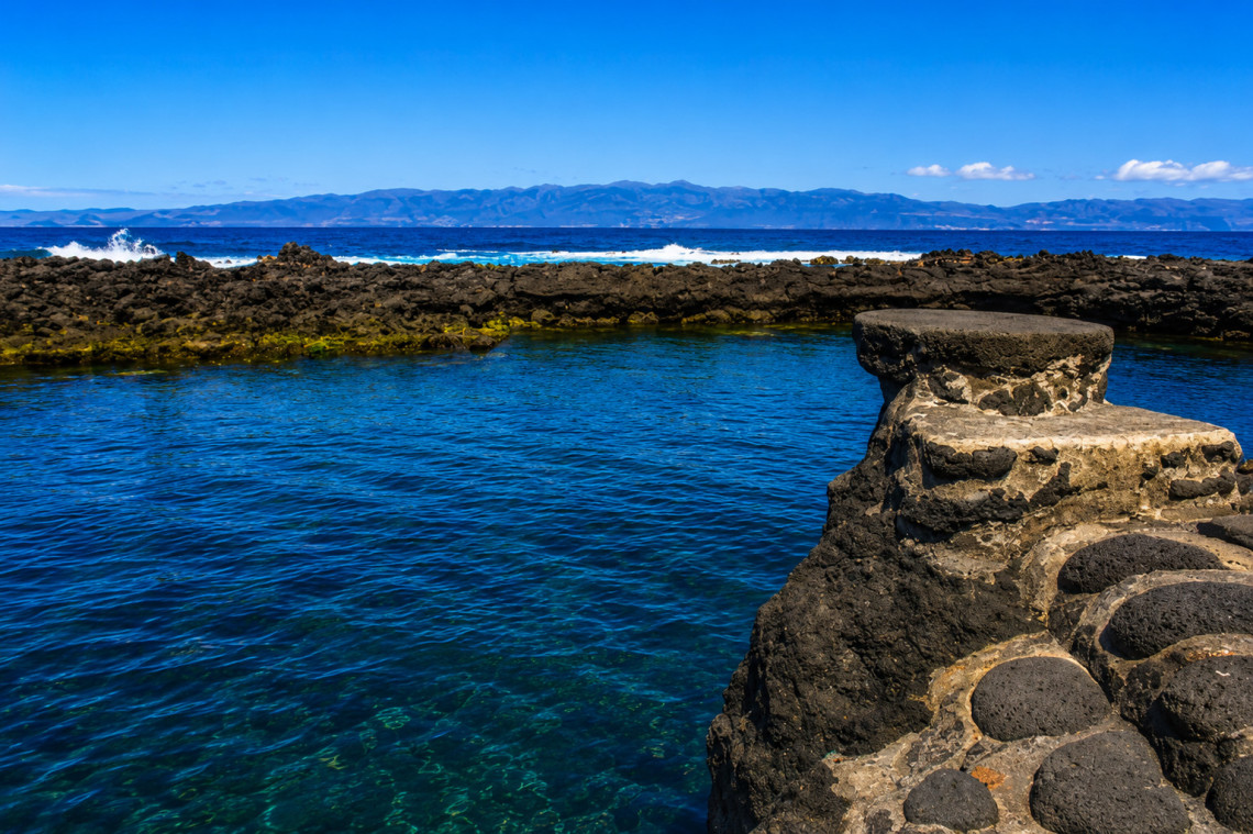 Po&ccedil;a Branca natural pool in Prainha on Pico Island, with calm Atlantic water enclosed by low black volcanic rock formations and stone access structures.
