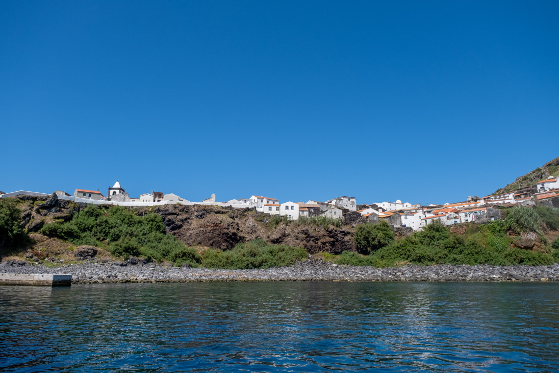 Vila do Corvo stretches above the rocky Atlantic shoreline of Corvo Island in the Azores, Portugal. Whitewashed houses with red-tiled roofs and the local church stand against the steep volcanic landscape.