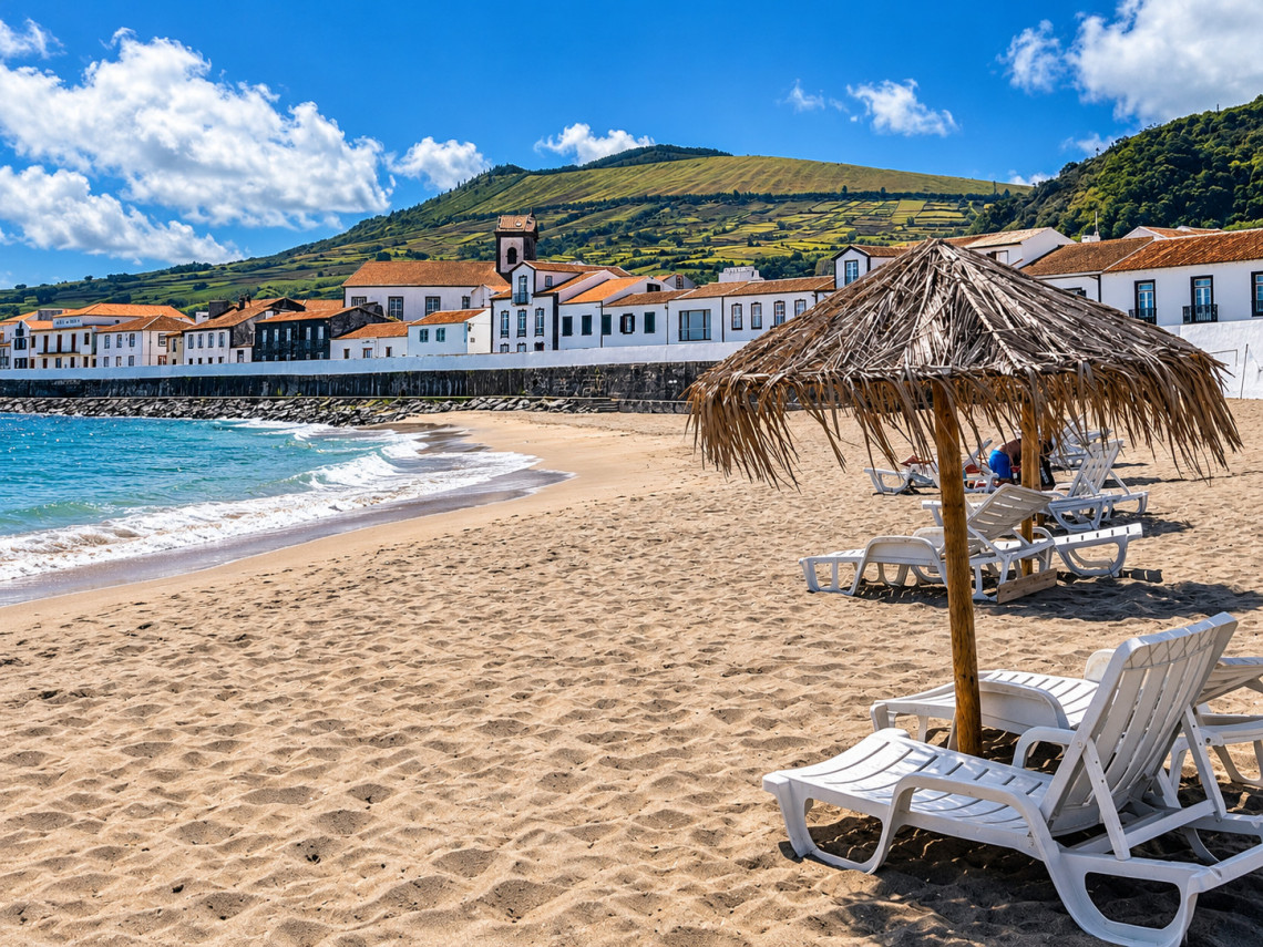 Praia de S&atilde;o Mateus on Graciosa Island, with a sandy shoreline, straw parasols and whitewashed waterfront buildings beneath the island&rsquo;s green agricultural slopes.