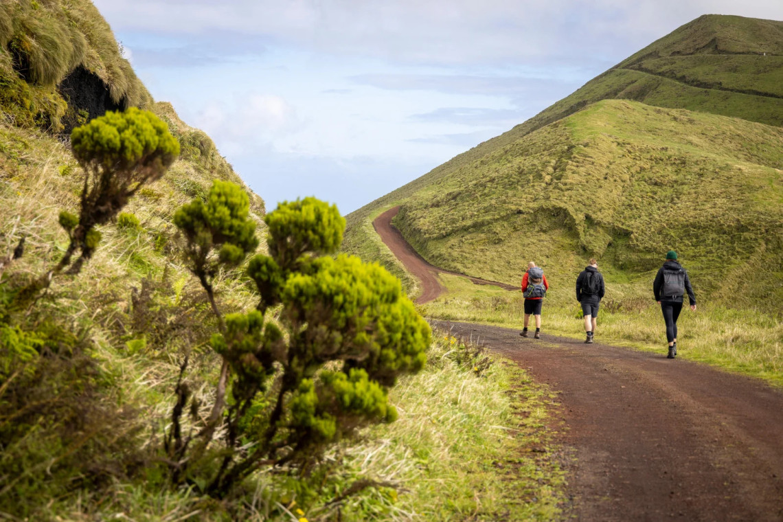 Hikers walking along a volcanic trail near Pico da Esperan&ccedil;a on S&atilde;o Jorge Island, surrounded by rolling green ridges and native vegetation.