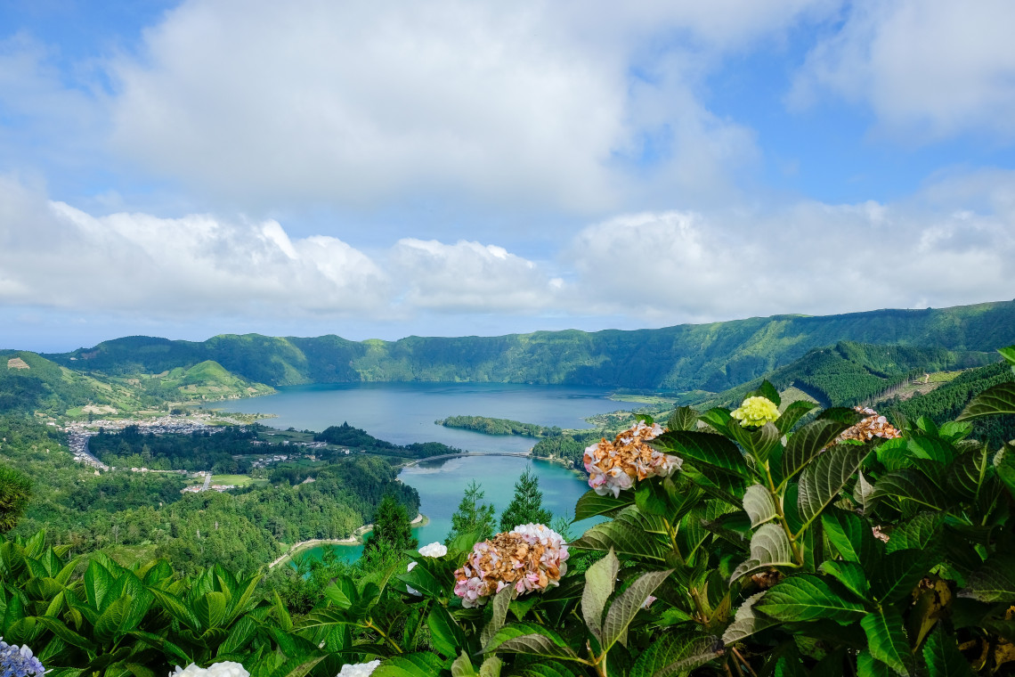 Panoramic view from Vista do Rei over the Sete Cidades caldera, with the volcanic lakes, village and green crater walls framed by hydrangeas.
