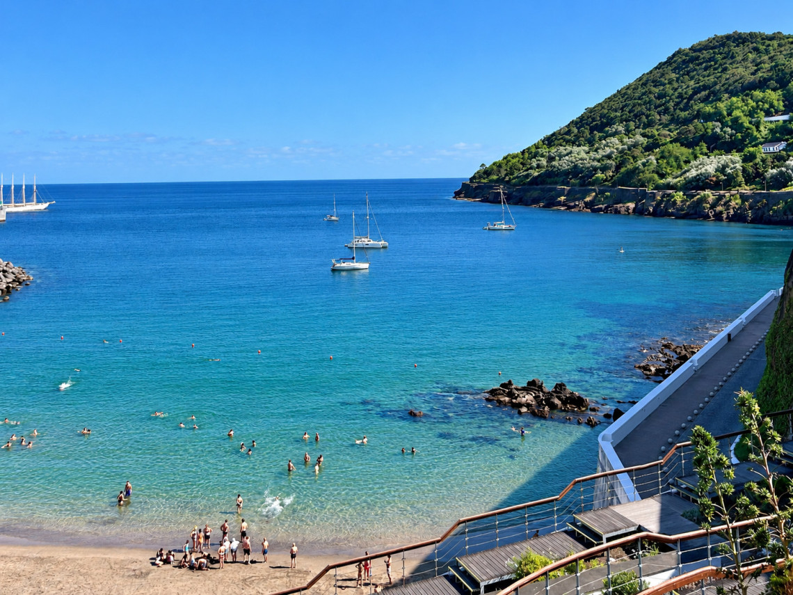 View of Prainha in Angra do Hero&iacute;smo on Terceira Island, with clear turquoise water, swimmers and sailboats in the sheltered bay beside Monte Brasil.