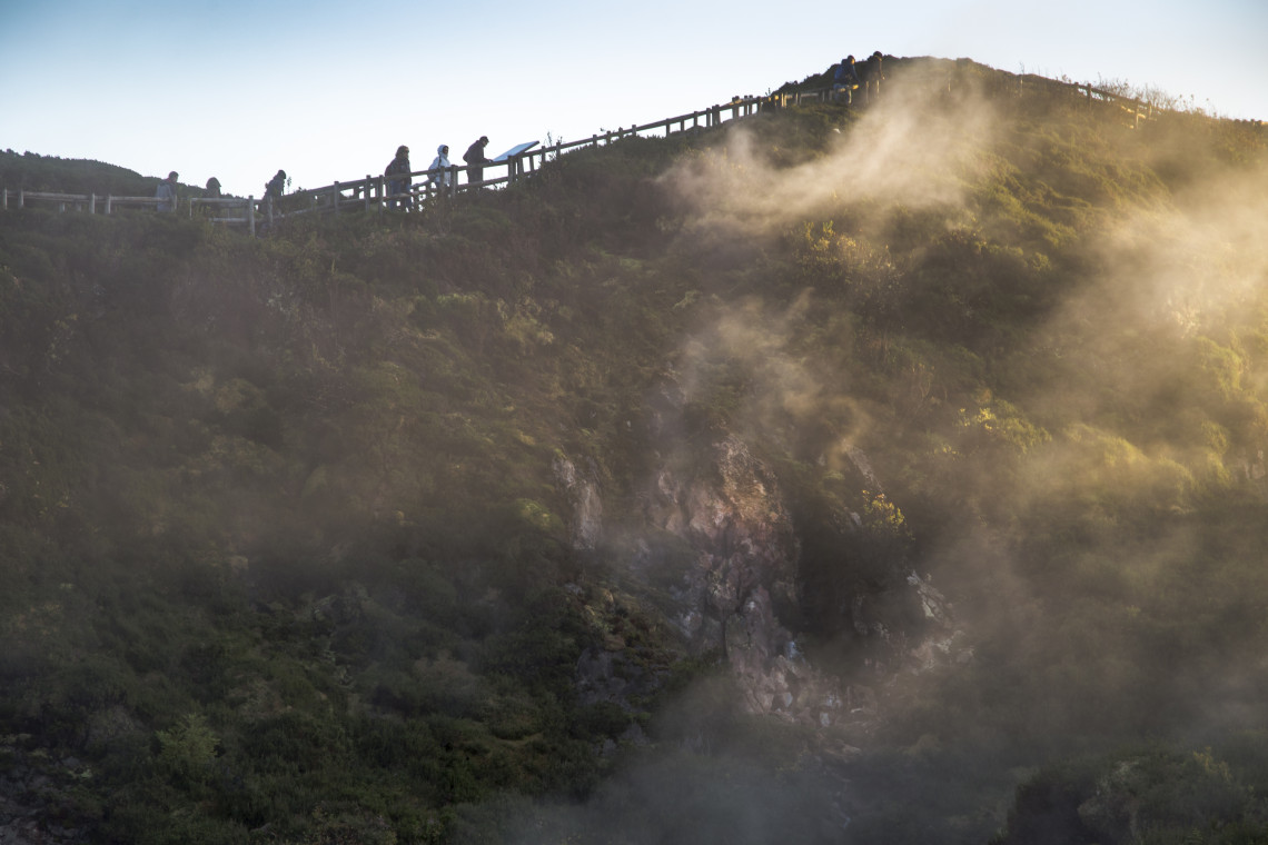 Steam rising from the volcanic landscape at Furnas do Enxofre on Terceira Island, with visitors walking along the elevated trail above the fumarolic field.