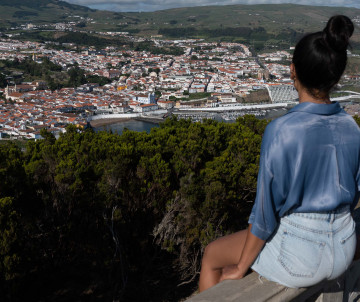 Visitor overlooking the historic city of Angra do Heroísmo from Monte Brasil on Terceira Island. Red-roofed buildings and the surrounding green landscape stretch across the view below.