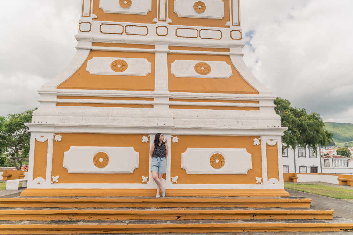 Woman leaning against the ornate yellow and white Alto da Memória monument at the viewpoint above Angra do Heroísmo, Terceira Island, Azores