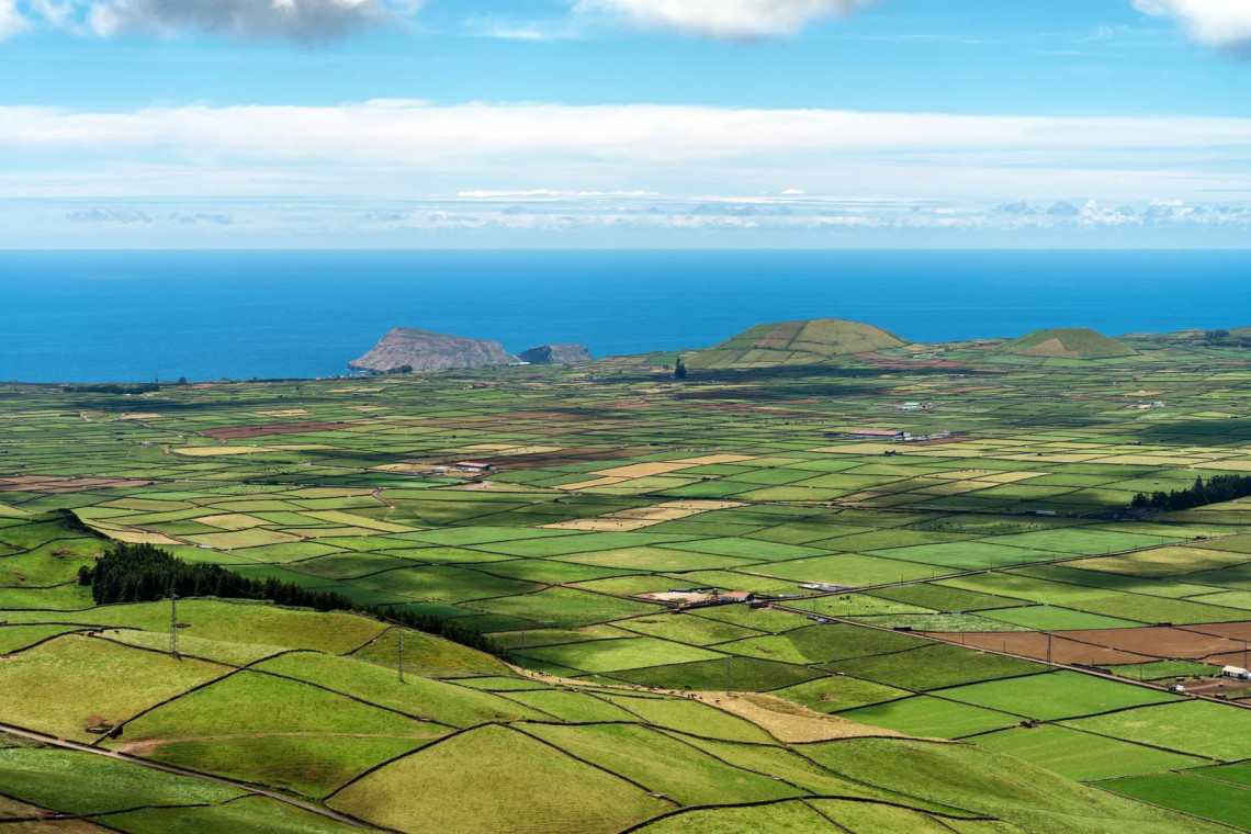 Aerial view from Miradouro da Serretinha overlooking the mosaic of green fields divided by basalt stone walls, volcanic cones, and the Atlantic Ocean coastline of Terceira Island, Azores