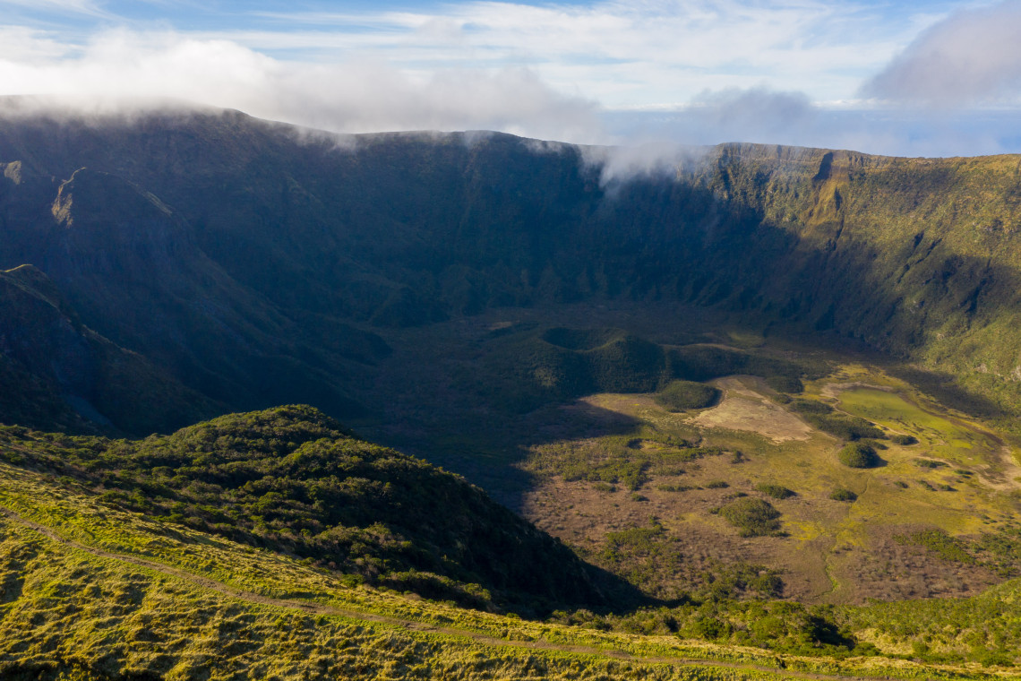 Aerial view of the vast Caldeira do Faial volcanic crater with steep green walls partially covered by cloud, Faial Island, Azores