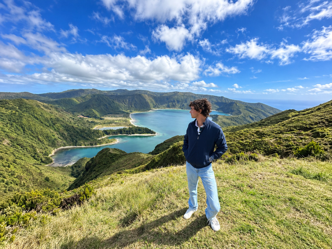 Visitor standing above Lagoa do Fogo on S&atilde;o Miguel Island, with the crater lake, smaller lagoons and green volcanic mountains beneath a bright blue sky.