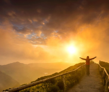 Visitor enjoying sunset from Miradouro da Boca do Inferno on São Miguel Island, with volcanic ridges and the Sete Cidades landscape illuminated by golden light.