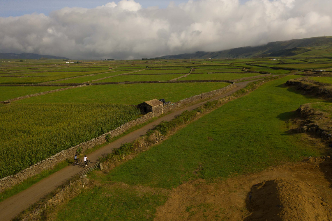 Rural landscape on Terceira Island with green agricultural fields divided by traditional volcanic stone walls, a country road and a small stone shelter beneath low clouds.