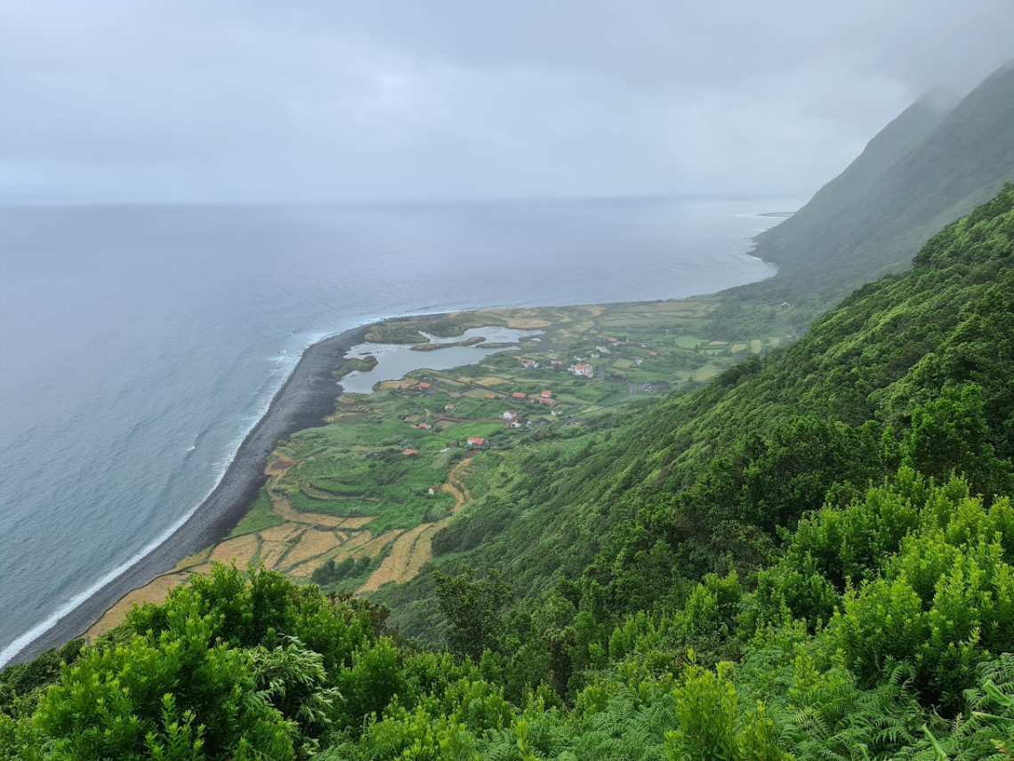 Elevated view of Faj&atilde; dos Cubres on S&atilde;o Jorge Island, showing its coastal lagoons, green fields and scattered houses between the Atlantic Ocean and steep forested cliffs.
