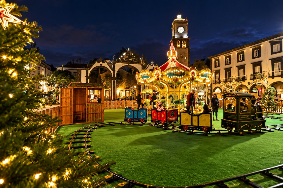 A Christmas village in central Ponta Delgada features an illuminated carousel, children's train, Christmas trees and festive lights near Portas da Cidade.