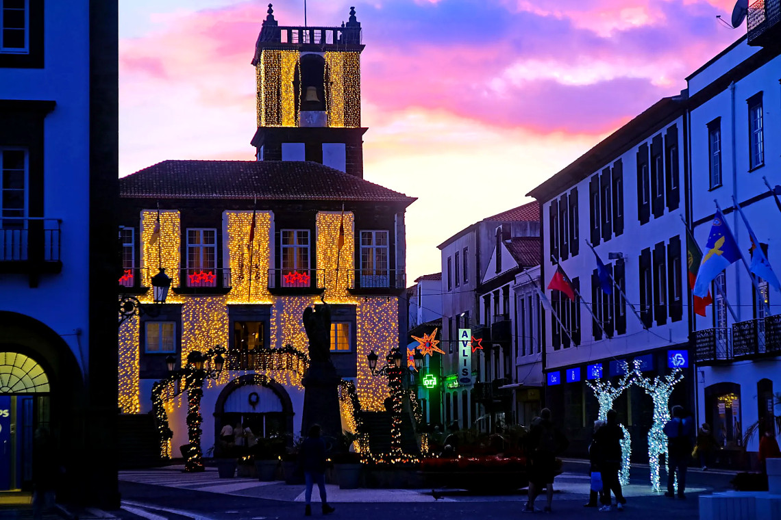 Ponta Delgada City Hall is covered in warm Christmas lights at dusk, with illuminated decorations extending through the surrounding historic streets.