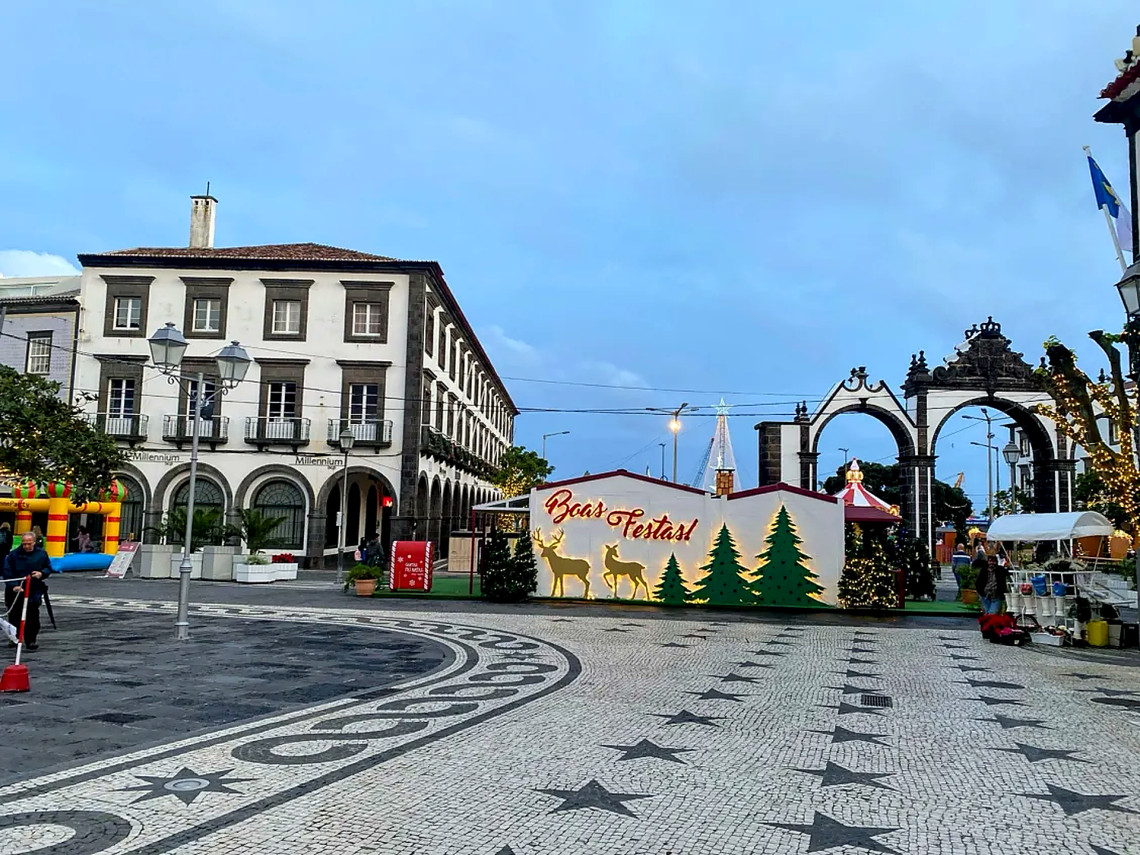 Christmas stalls and seasonal decorations fill the historic center of Ponta Delgada, with Portas da Cidade visible behind the festive market area.