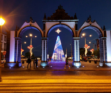 The historic Portas da Cidade in Ponta Delgada illuminated for Christmas, with a large light-covered Christmas tree framed by the three arches.