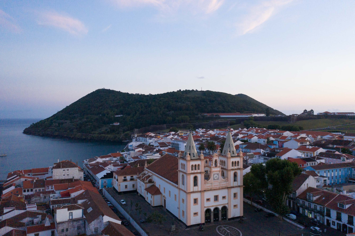 Aerial view of S&eacute; Cathedral in the historic center of Angra do Hero&iacute;smo, with red-roofed buildings and Monte Brasil rising behind the city.