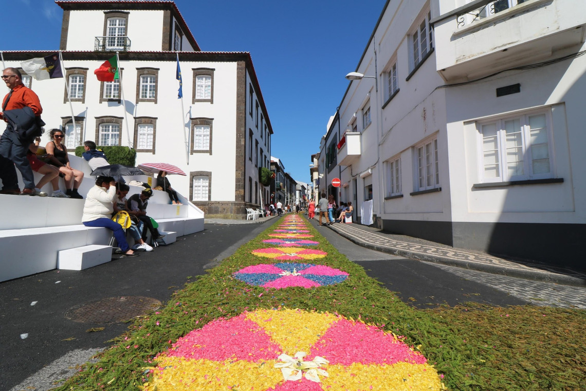 Colorful flower carpets arranged along a street in Ponta Delgada for the Festas do Senhor Santo Cristo dos Milagres, with spectators gathered beside the decorated route.