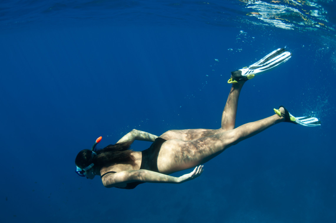 Snorkeler wearing a mask, snorkel and fins swimming through the deep blue waters surrounding Santa Maria Island in the Azores.