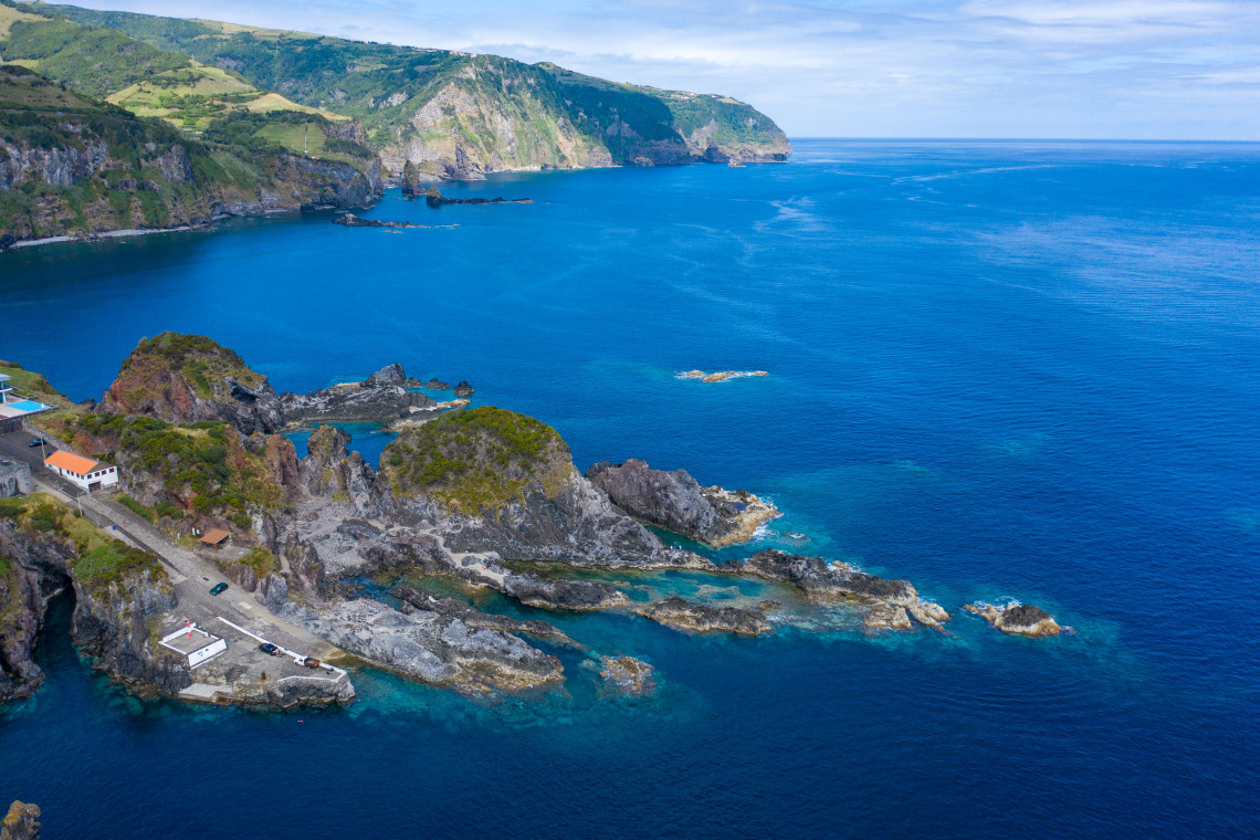 Aerial view of the volcanic coastline of Flores Island in the Azores, with natural seawater pools, rocky formations and steep green cliffs beside the Atlantic Ocean.