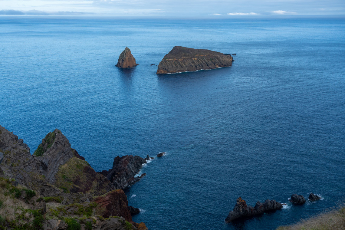 View of Ilh&eacute;u de Baixo off Graciosa Island, showing an elongated volcanic islet and a tall isolated sea stack rising from the Atlantic Ocean.