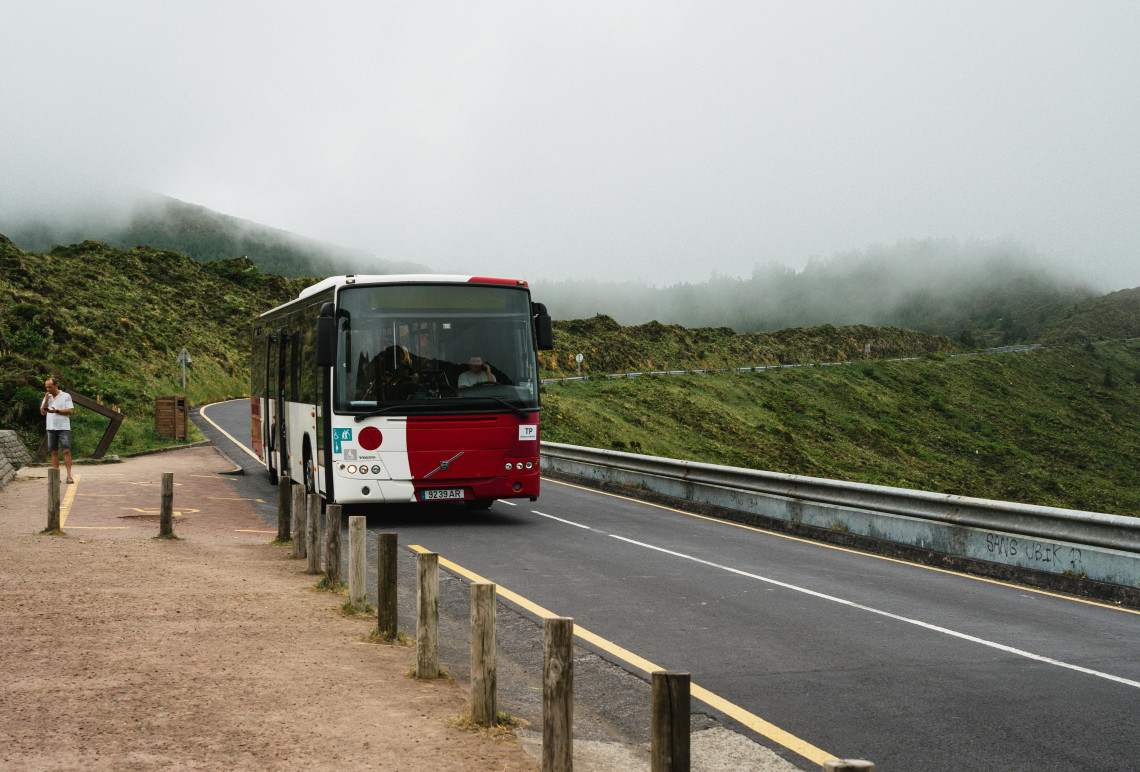 Shuttle bus traveling along the mountain road to Lagoa do Fogo on S&atilde;o Miguel Island, surrounded by green slopes and low mist.