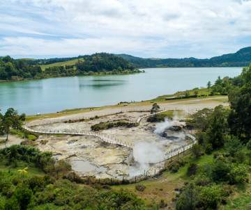 View of the geothermal fumaroles beside Lagoa das Furnas on São Miguel Island, with steam rising from the volcanic ground beside the lake and surrounding green landscape.