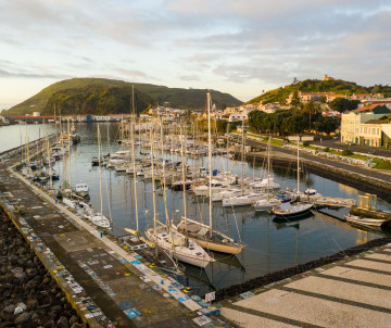 Aerial view of Horta Bay on Faial Island, Azores, Portugal, showing the marina, waterfront and whitewashed city buildings extending across the green hillside.