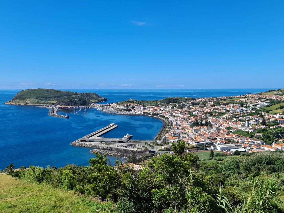 Panoramic view of Horta on Faial Island, showing the marina, harbor, red-roofed city center and Atlantic coastline.