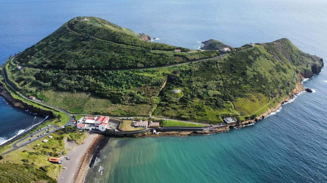 Aerial view of Monte da Guia on Faial Island, showing its green volcanic slopes, coastal road and the sheltered waters of Porto Pim Bay.