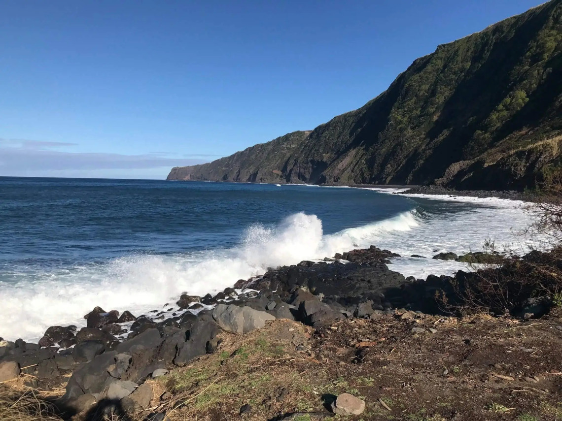 Atlantic waves breaking against black volcanic rocks below the steep green cliffs of the Praia do Norte coastline on western Faial Island.