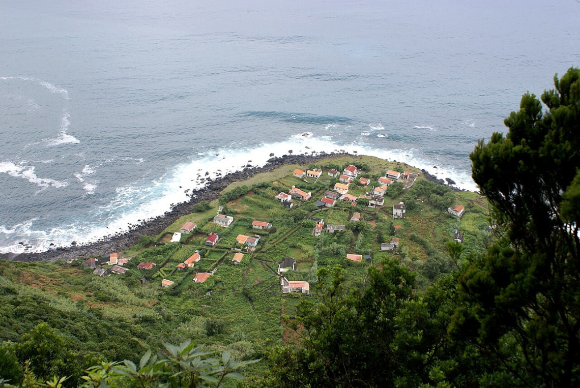 Elevated view of Faj&atilde; de Jo&atilde;o Dias on S&atilde;o Jorge Island, showing scattered houses and cultivated plots on a narrow coastal platform surrounded by the Atlantic.