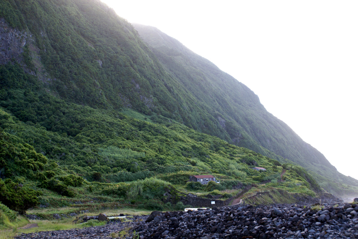 Faj&atilde; dos Tijolos on S&atilde;o Jorge Island, with a small rural property and cultivated land at the base of towering green cliffs beside the Atlantic coast.