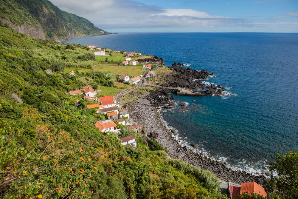 Faj&atilde; das Almas on S&atilde;o Jorge Island, showing traditional red-roofed houses, cultivated slopes and a dark volcanic shoreline beside the Atlantic Ocean.