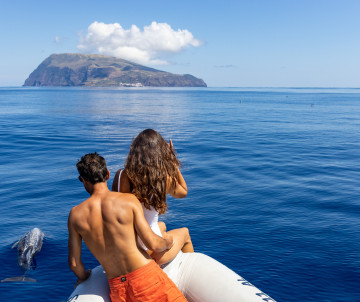 Couple sitting on the bow of a ferry boat looking toward Corvo Island rising from the Atlantic Ocean, Azores inter-island ferry, Portugal