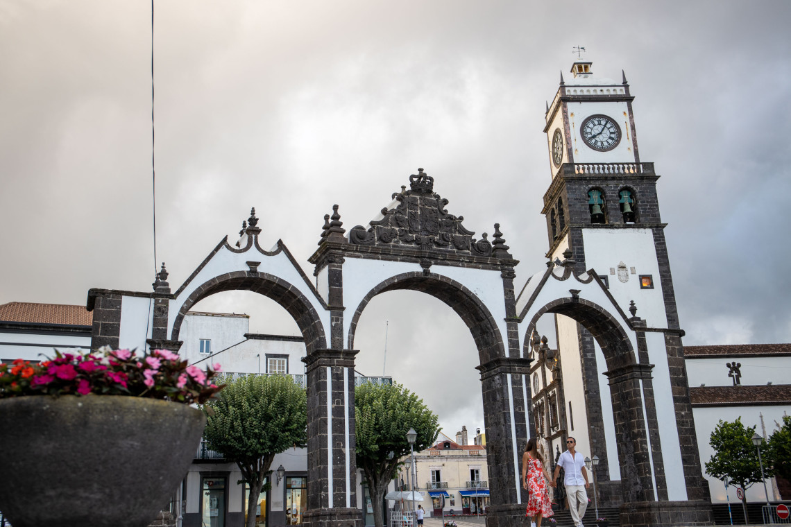 The black-and-white stone arches of Portas da Cidade stand beside the historic clock tower in central Ponta Delgada, with visitors walking through the landmark square.