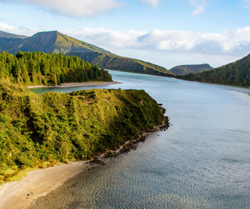 View across Lagoa do Fogo on São Miguel Island, surrounded by steep green volcanic slopes, forested terrain and the calm waters of the crater lake.