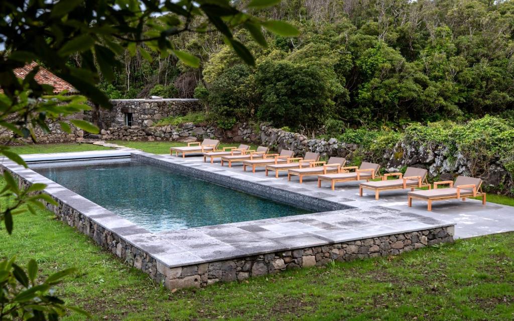 Outdoor swimming pool at Aldeia da Cuada in Faj&atilde; Grande on Flores Island, Azores, Portugal. Sun loungers line the volcanic-stone pool, surrounded by traditional stone walls and dense woodland.