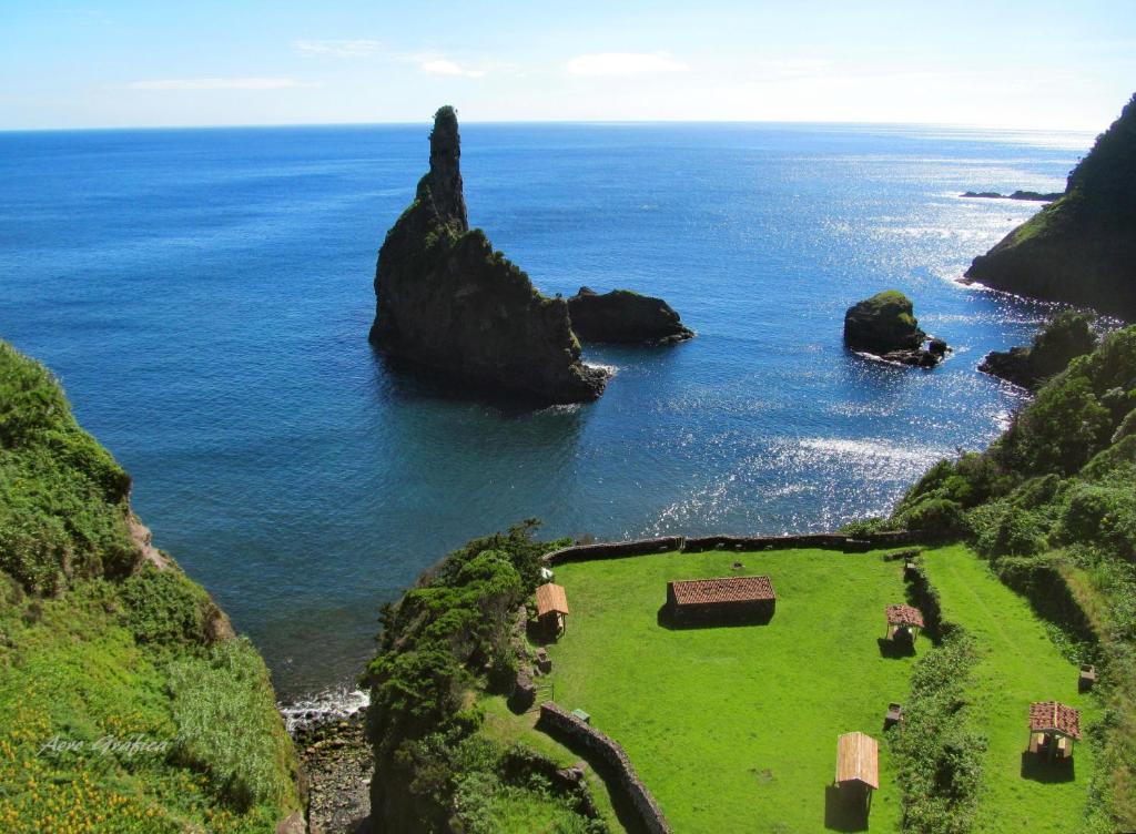Elevated view of Ba&iacute;a da Alagoa near Cedros on Flores Island, Azores, Portugal. Tall volcanic sea stacks rise from the Atlantic beside a sheltered bay, green lawns and small stone buildings.