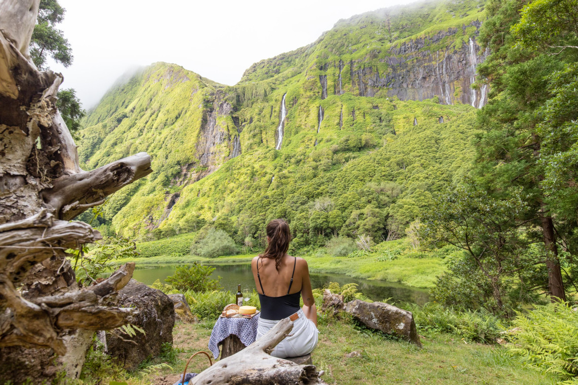 : A visitor looks toward the lagoon and waterfalls of Po&ccedil;o da Ribeira do Ferreiro near Faj&atilde; Grande on Flores Island, Portugal. Multiple cascades descend the densely vegetated volcanic cliffs surrounding the water.