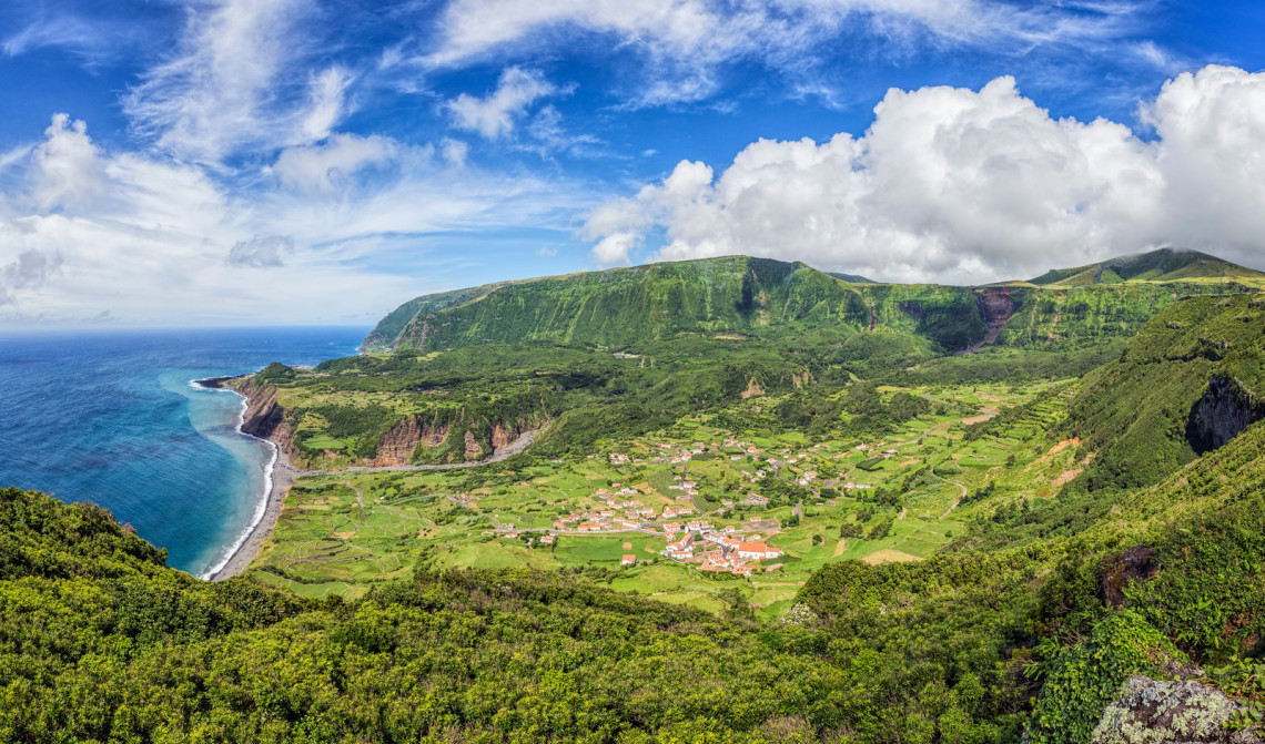 Panoramic view from Miradouro do Portal over Faj&atilde;zinha on Flores Island, Azores, Portugal. Patchwork fields and red-roofed houses occupy the coastal valley beneath green cliffs beside the Atlantic Ocean.