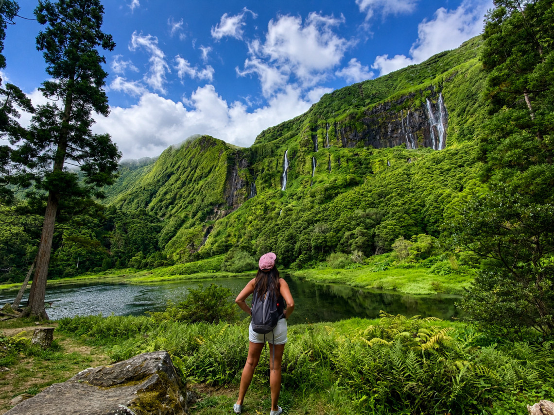 A hiker overlooks the lagoon at Po&ccedil;o da Ribeira do Ferreiro near Faj&atilde;zinha on Flores Island in the Azores, Portugal. Multiple waterfalls descend from steep, vegetation-covered cliffs into the calm water