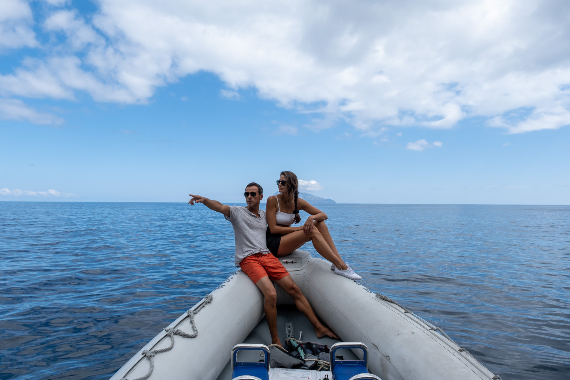 A couple sits at the bow of an inflatable boat during an Atlantic excursion from Flores Island in the Azores, Portugal. Corvo Island appears on the horizon as they travel between the western Azorean islands.
