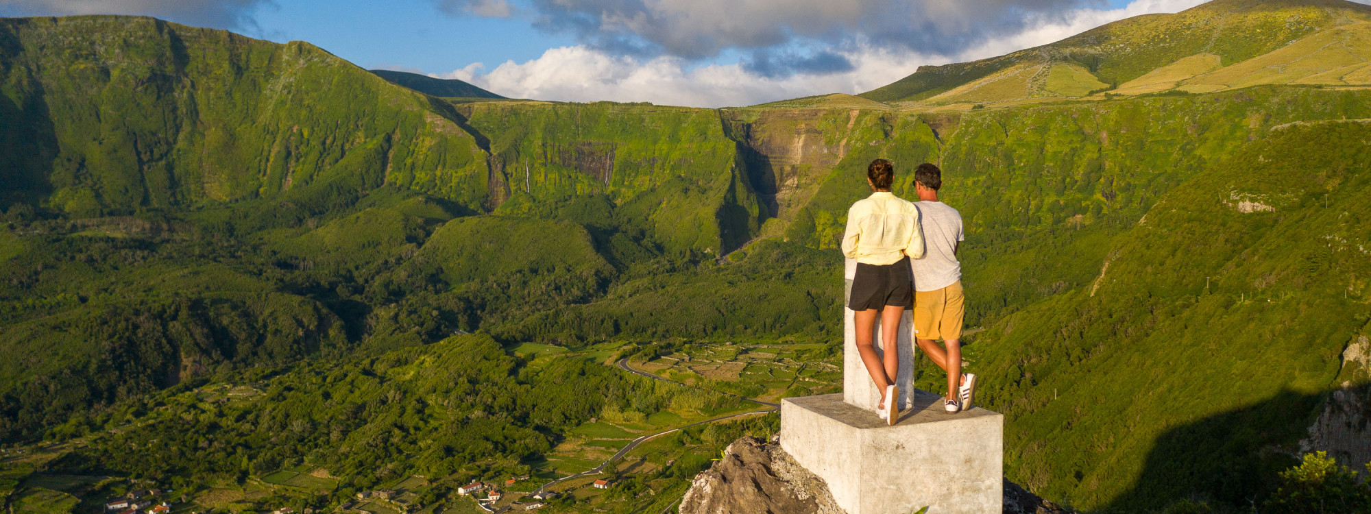 Visitors enjoying a boat tour beneath the volcanic sea cliffs of Corvo Island, Azores, Portugal. The dramatic Atlantic coastline features towering rock formations, sea caves, and rugged coastal landscapes.