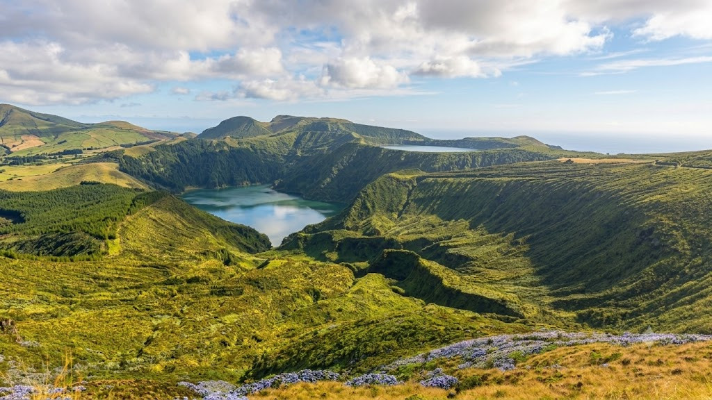 Lagoa Funda fills a deep volcanic crater on Flores Island in the Azores, Portugal. Green ridges and crater walls surround the lake, with the Atlantic Ocean visible beyond the island&rsquo;s highlands.