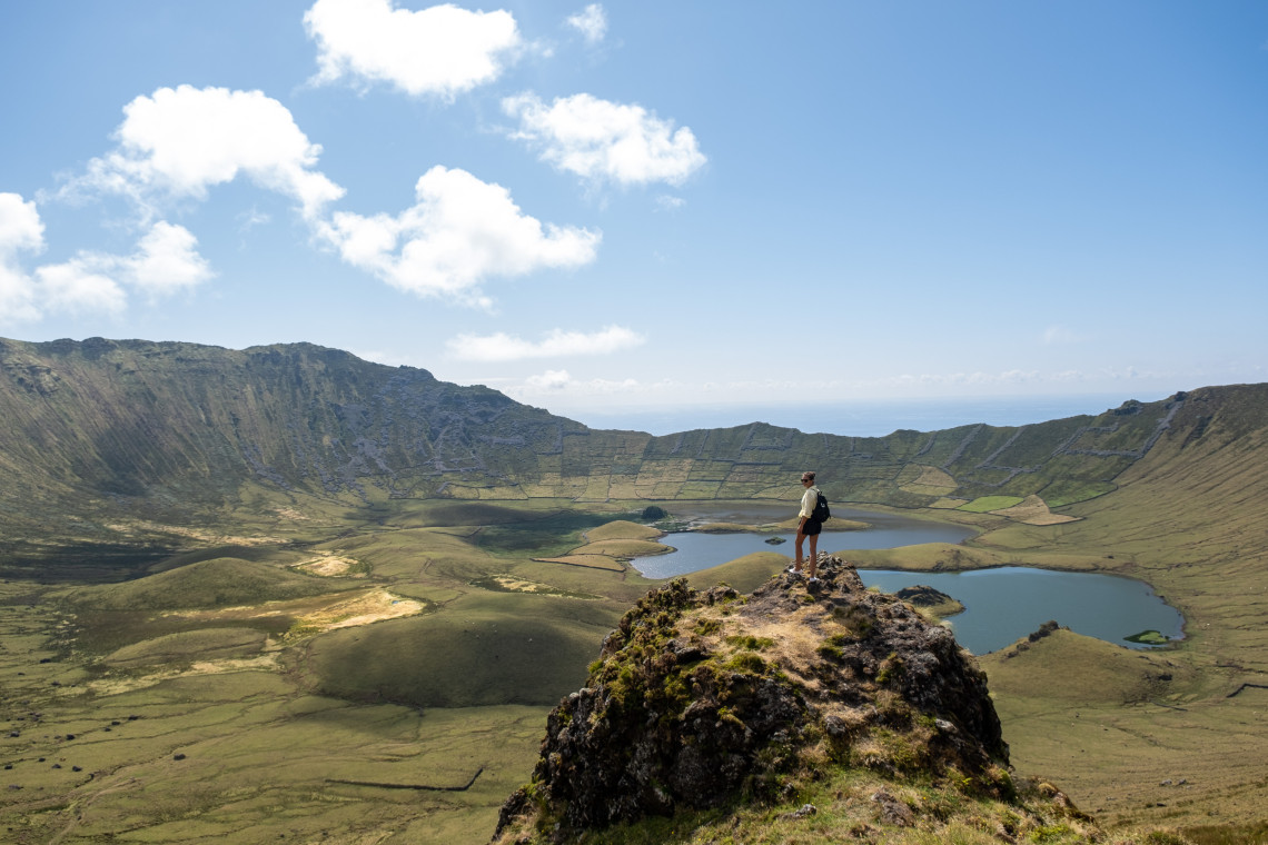 A hiker stands above the Caldeir&atilde;o crater on Corvo Island in the Azores, Portugal. Small lakes and volcanic cones occupy the broad green floor of the island&rsquo;s central caldera.