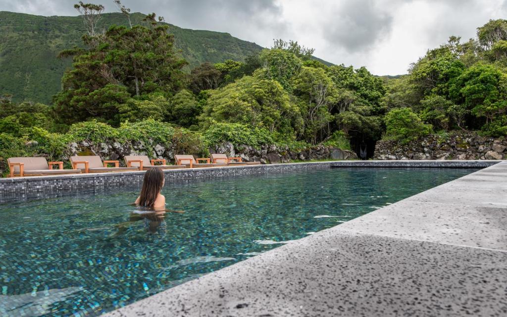 A guest swims in the outdoor pool at Aldeia da Cuada near Faj&atilde; Grande on Flores Island, Azores. The pool is surrounded by stone walls, sun loungers, dense vegetation and the island&rsquo;s steep green hills.
