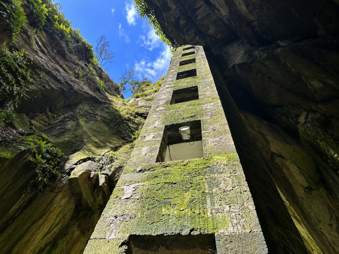 View upward along the stone access tower at Furna do Enxofre on Graciosa Island, built into the volcanic opening and surrounded by moss-covered rock walls. Visitors descend 183 steps to reach the cave interior.